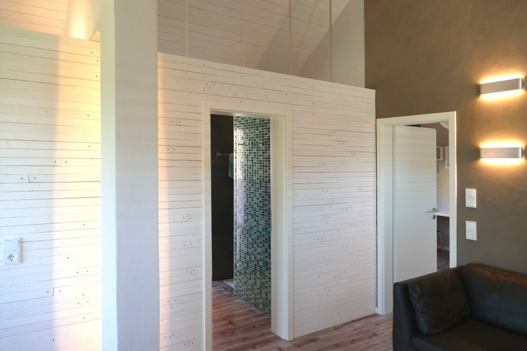 Un intérieur moderne avec un mur en bois, un canapé de couleur sombre et une zone de douche carrelée.