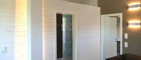 A modern interior with a wooden wall, a dark-colored sofa, and a tiled shower area.