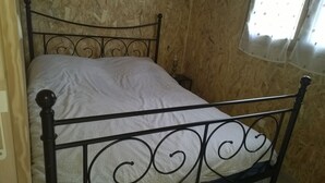 Una cama con estructura metálica y colcha estampada en una habitación con paredes de madera.