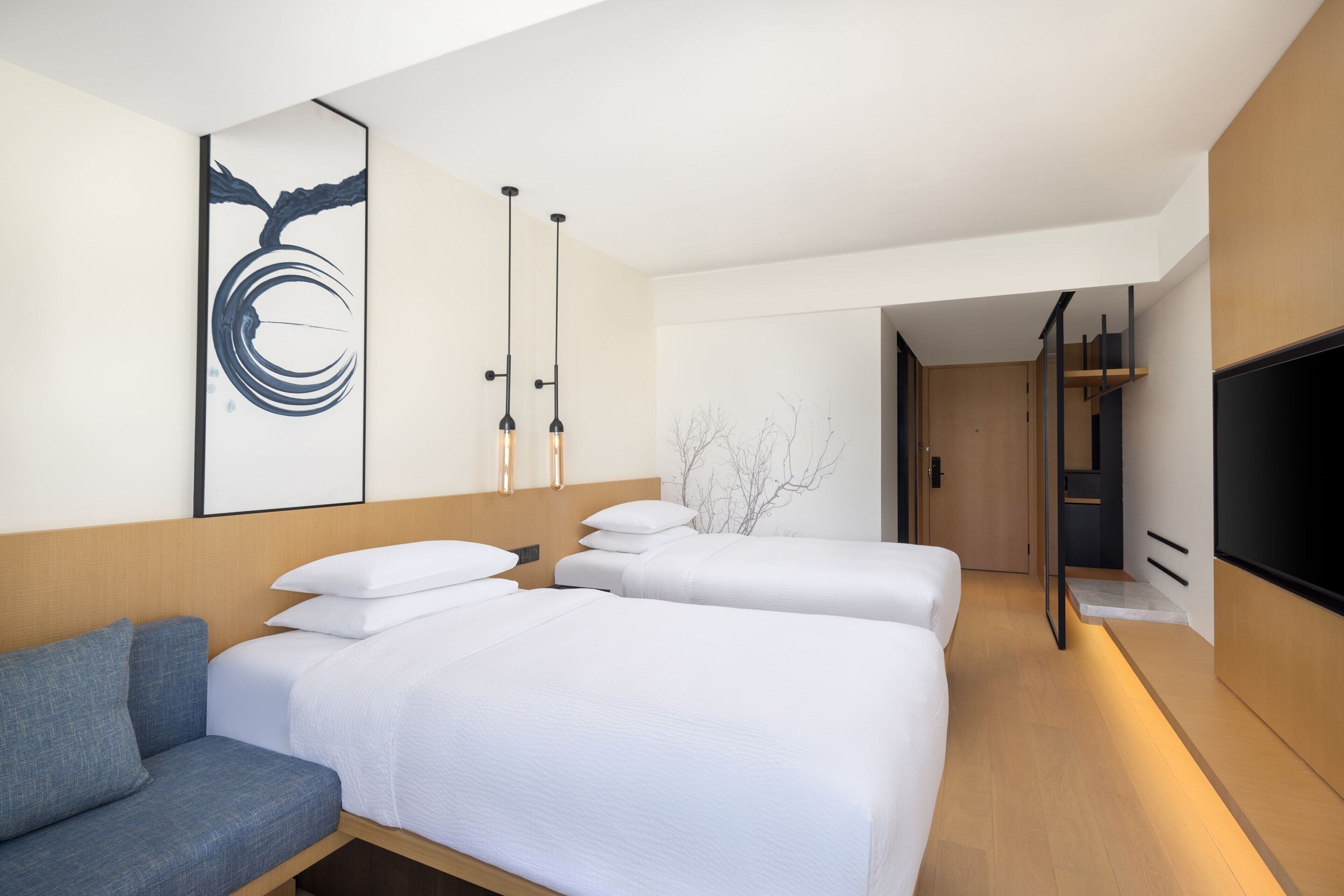 Habitación de hotel con dos camas, un sofá, un televisor y una obra de arte moderna en la pared.
