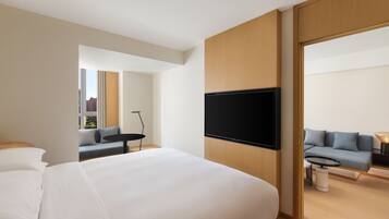 Quarto de hotel moderno com uma cama grande, televisão de tela plana na parede, sofá e uma pequena mesa.