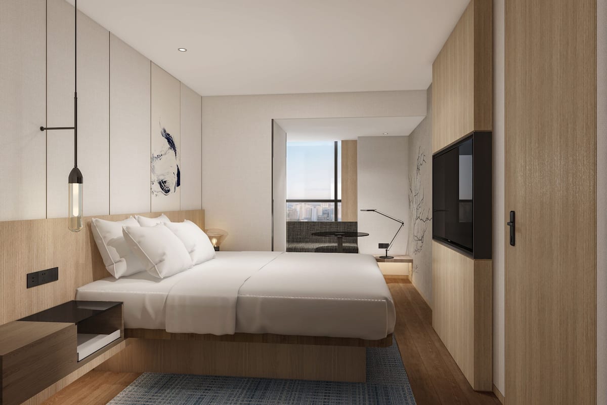 Ein modernes Schlafzimmer mit einem großen Bett, Nachttischen, einem Fernseher und Blick auf die Stadt.