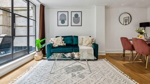 Un salon moderne avec un canapé de couleur turquoise, une table basse en verre et une grande fenêtre.
