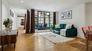 Un salon moderne avec un canapé de couleur turquoise, une table basse et une vue sur l’extérieur, accessible par une porte vitrée.