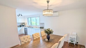 Un coin repas comprenant une table en bois, six chaises rembourrées, un vase avec des fleurs et un lustre.