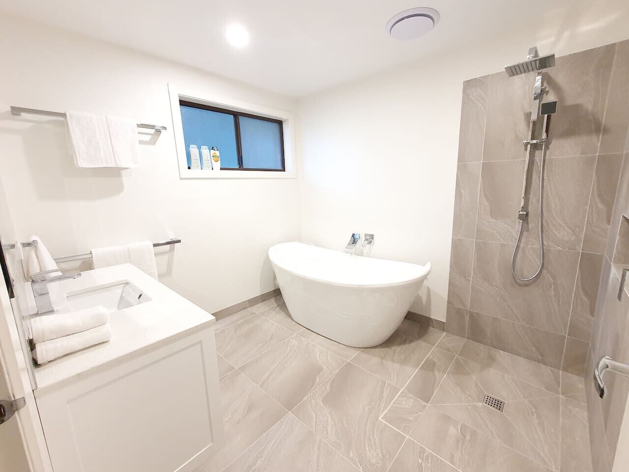Een moderne badkamer met een vrijstaand bad, een douche en een raam met flessen op de vensterbank.