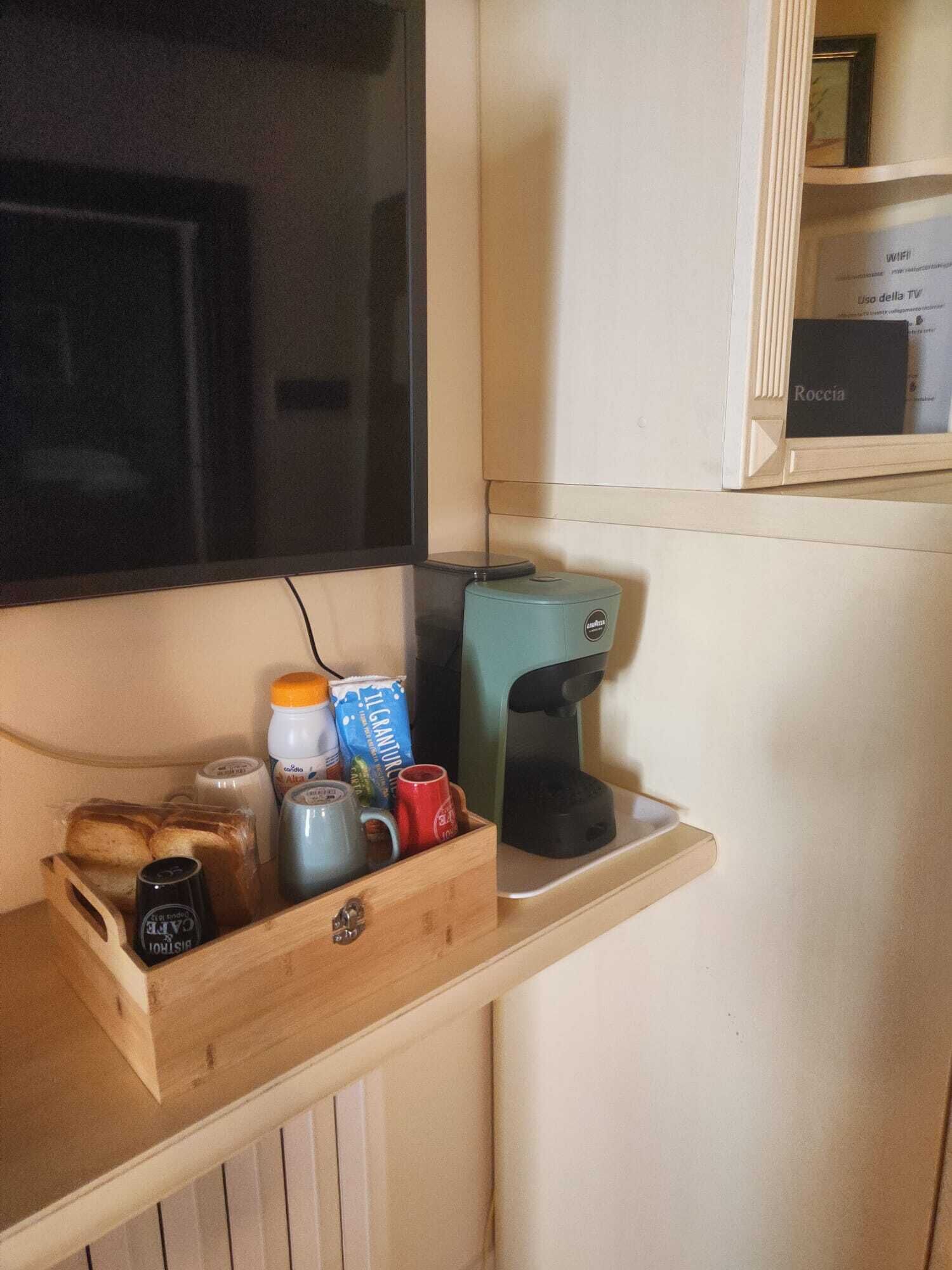 A kitchenette with a coffee maker, a wooden bread box, and various food items.