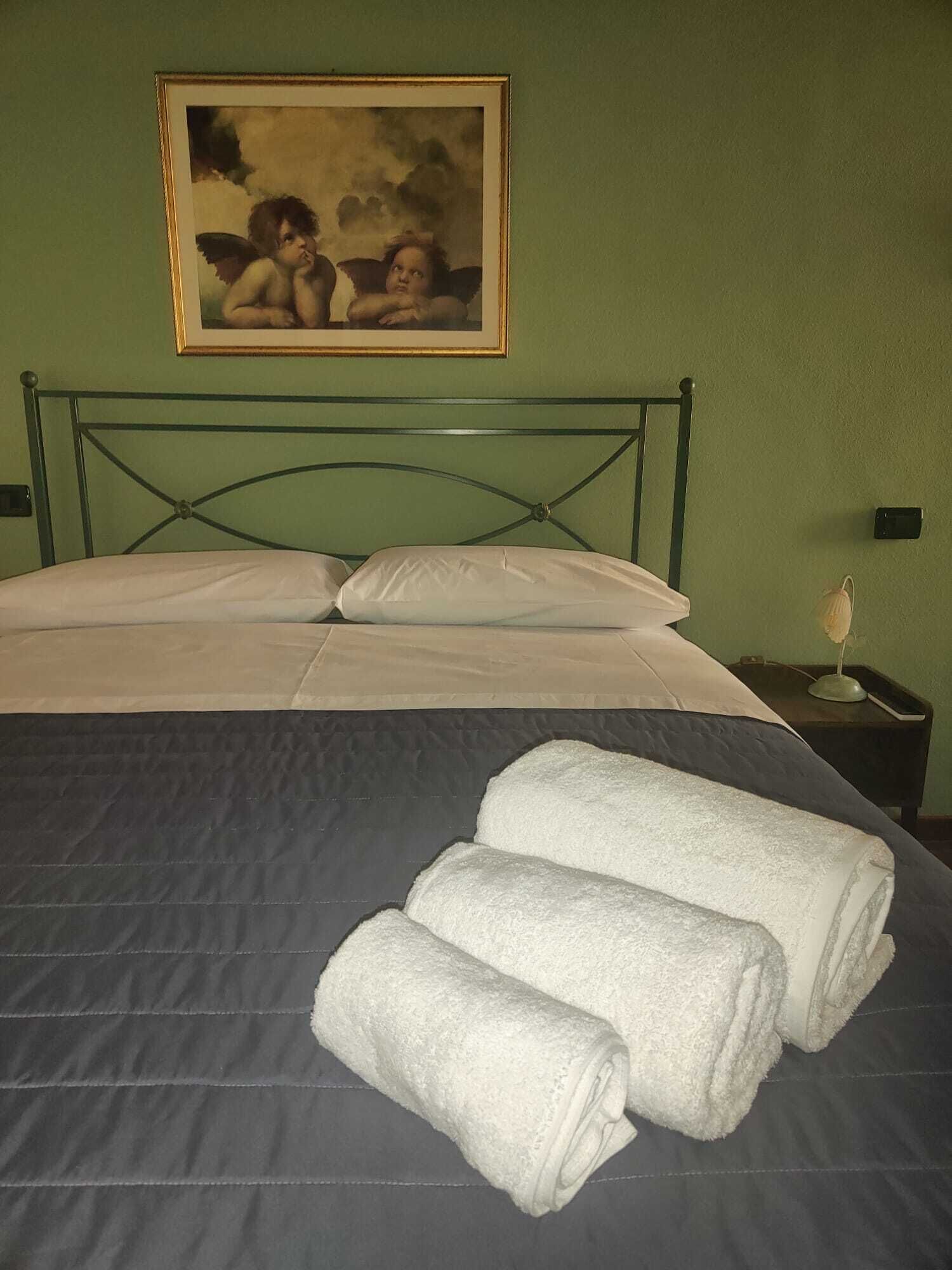Een net opgemaakt bed met witte lakens en twee opgerolde handdoeken.