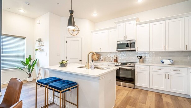 A modern kitchen with white cabinets, a central island with stools, stainless steel appliances, and a pendant light. - New Lux Home Steps to AT&T + Globe Life w/ Parking (Arlington)