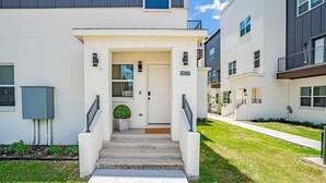A modern apartment building with a white facade, a front door, and a small garden area. - New Lux Home Steps to AT&T + Globe Life w/ Parking (Arlington)