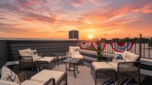 A rooftop patio with wicker furniture, a glass table, and a view of the sunset. - New Lux Home Steps to AT&T + Globe Life w/ Parking (Arlington)