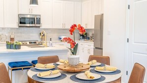 A modern kitchen with white cabinets, a stainless steel refrigerator, and a central island with a vase of red flowers. - New Lux Home Steps to AT&T + Globe Life w/ Parking (Arlington)