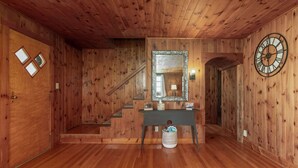A wooden interior with a staircase, a mirror, and a clock on the wall.