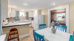 A modern kitchen with a central island, white cabinets, and a dining area with blue chairs.