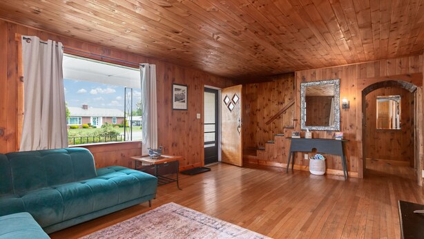 A wooden-paneled room with a sofa, a small table, a mirror, and a view of the outside.
