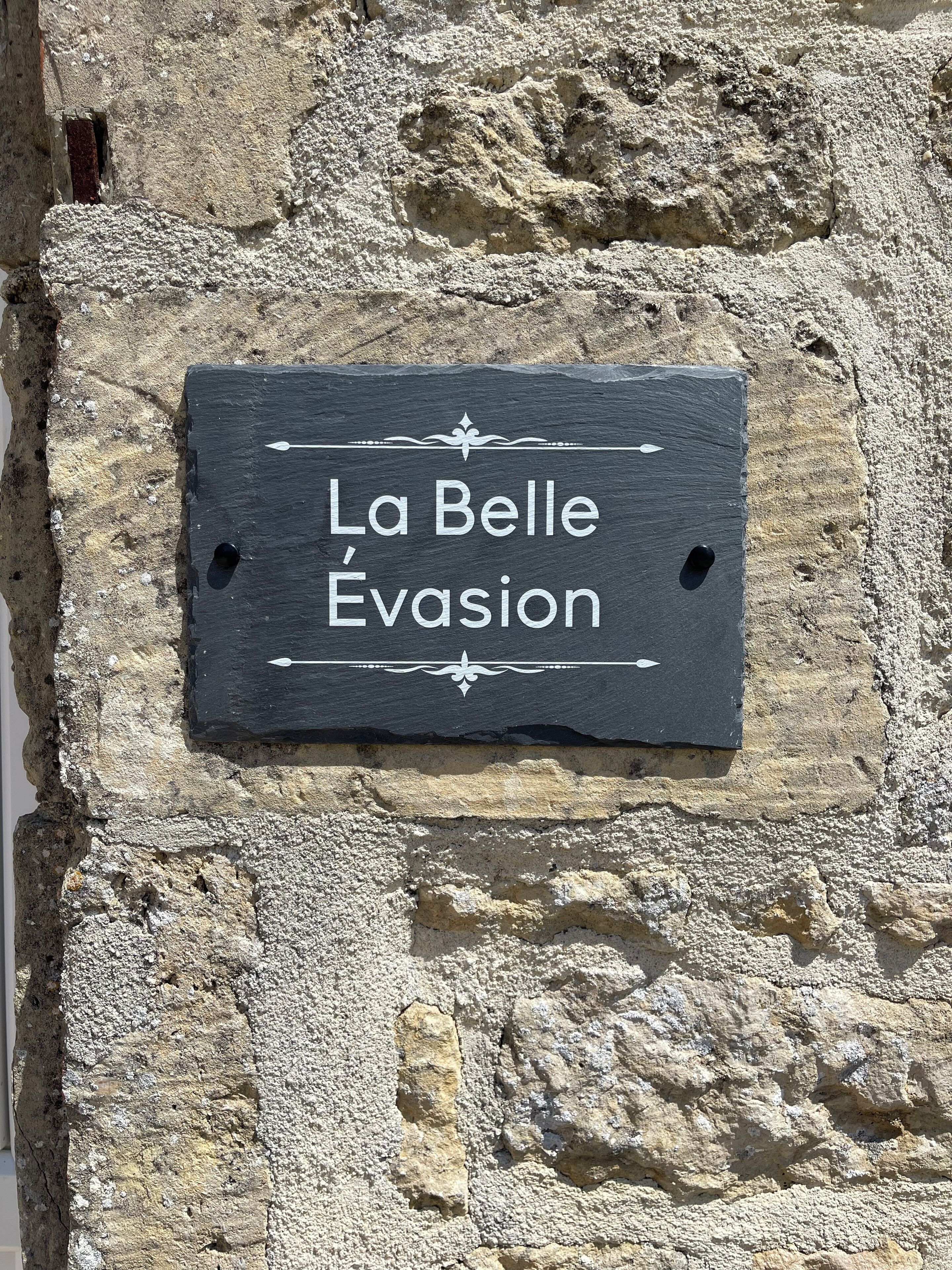A slate sign with the text 'La Belle Evasion' mounted on a stone wall.