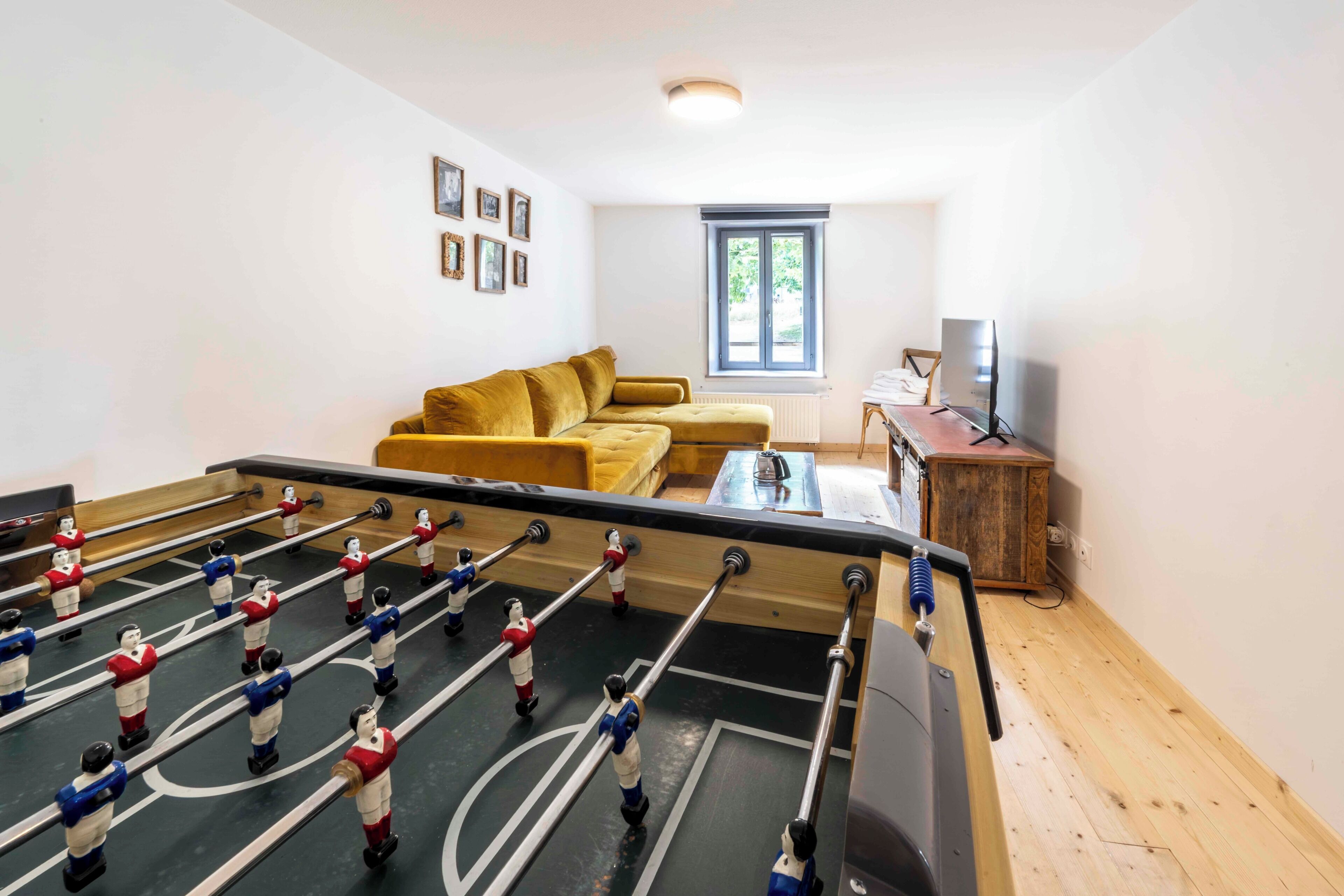 A room with a foosball table, a sofa, a television, and a window.