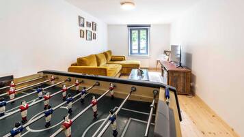 A room with a foosball table, a sofa, a television, and a window.