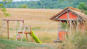 A rustic wooden playhouse with a slide and swings in a grassy field. - Gîte L'instant Vosges, private wellness area (Aydoilles)