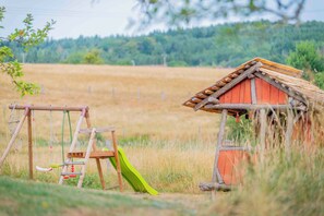 A rustic wooden playhouse with a slide and swings in a grassy field.