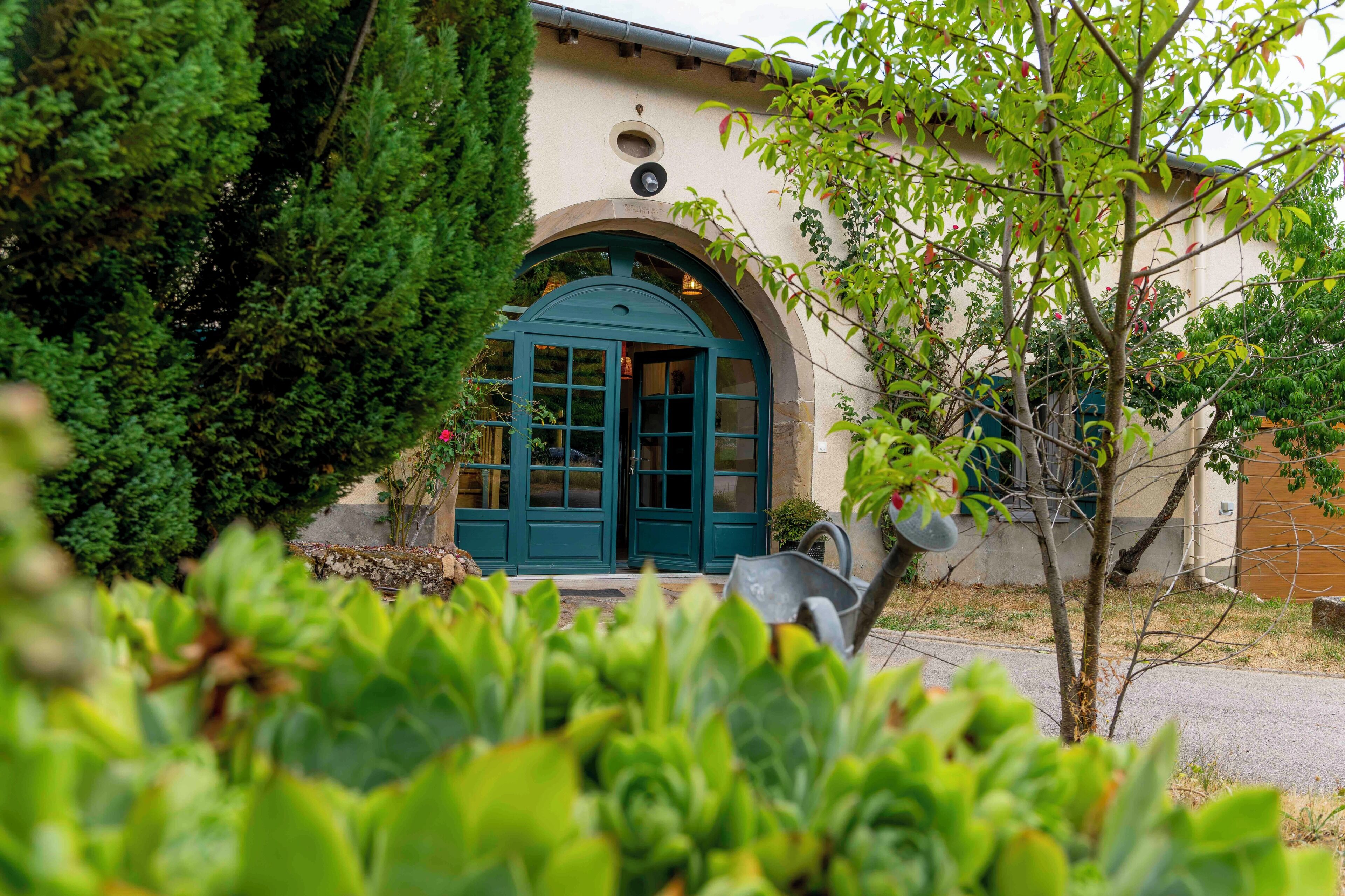 A building with a green door and a small window, surrounded by greenery.