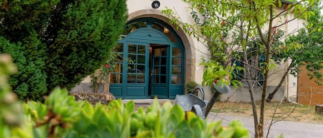 A building with a green door and a small window, surrounded by greenery.