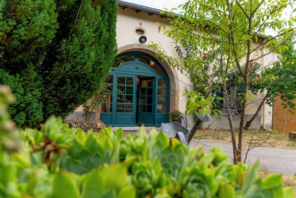 A building with a green door and a small window, surrounded by greenery.