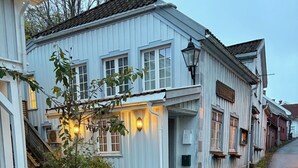 A white building with a porch and multiple windows, a street lamp, and a small tree in front.