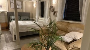 A cozy bedroom with a bed, a sofa, and a potted plant.