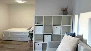 Ein modernes Schlafzimmer mit einem Bett, einem weißen Konsolentisch, einem grauen Sofa und einer weißen Regaleinheit.