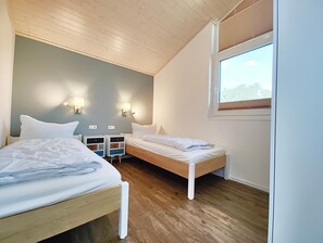 Quarto com duas camas, mesas de cabeceira, luminárias na parede e janela com persianas.