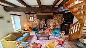 Un salon chaleureux avec une cheminée en pierre, des poutres apparentes et des fauteuils confortables.