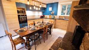 Une cuisine moderne avec des meubles en bois, un four encastré et un coin repas agrémenté d’une cheminée en pierre.