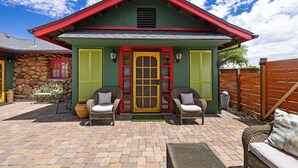 A house with a red roof, green walls, and a yellow door. There are two wicker chairs with cushions outside.
