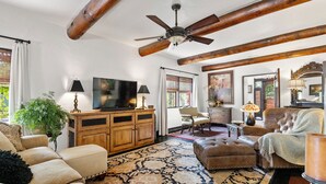A spacious living room with a large television, wooden beams, a patterned rug, and a comfortable seating area.