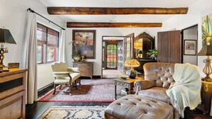 A spacious living room with a large leather sofa, a wooden coffee table, and a patterned rug. There is a wooden cabinet and a chair with a decorative cushion.