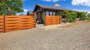 A rustic cabin with a wooden fence, a stone chimney, and a gravel driveway.