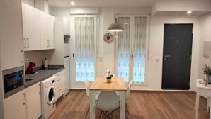 Una cucina moderna con mobili bianchi, forno integrato e lavatrice. Si nota un tavolo da pranzo con sedie e una lampada a sospensione sopra.
