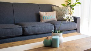 A grey sofa with a cushion labeled "maui," a small potted plant, and two candles on a wooden table.