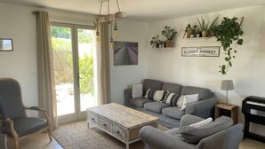 A living room with a grey sofa, a wooden coffee table, a grey armchair, a piano, and a wall-mounted shelf with plants.