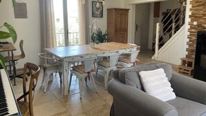 A dining area with a wooden table and chairs, a piano, and a grey sofa.