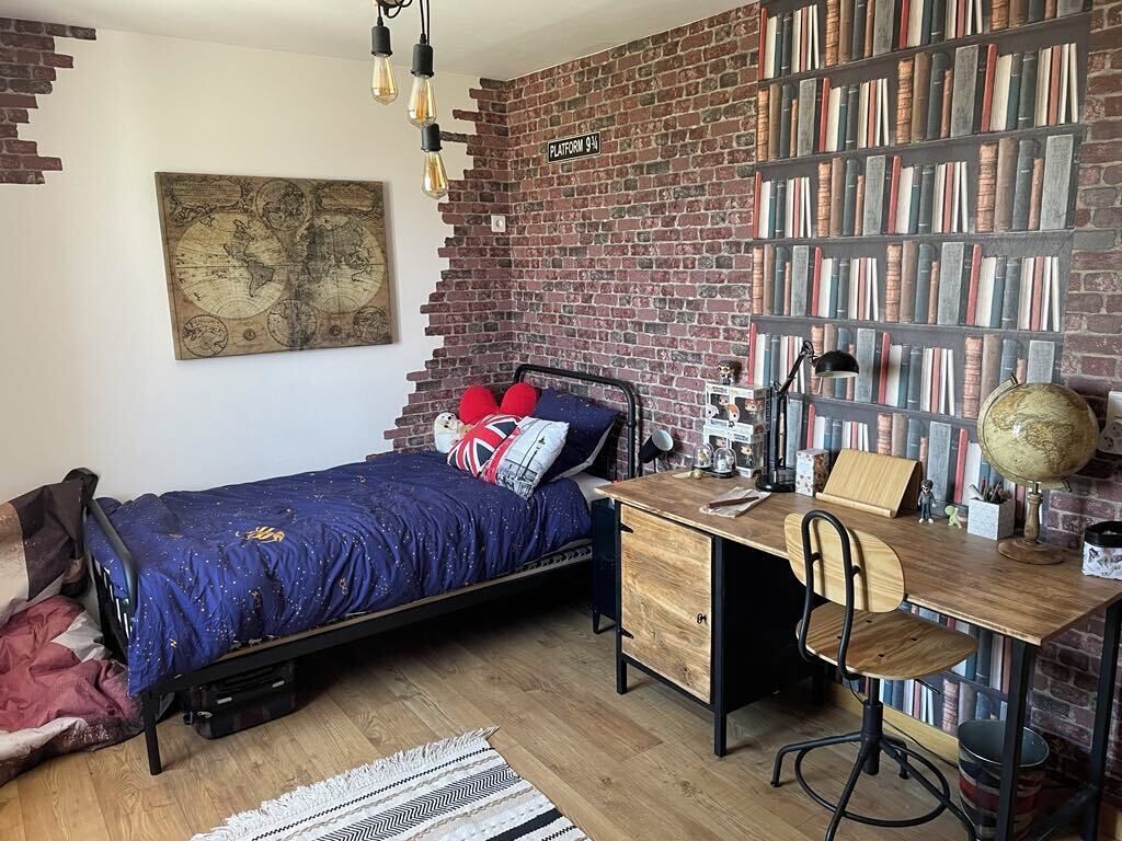 A bedroom with a bed, a desk, a bookshelf, and a map on the wall.