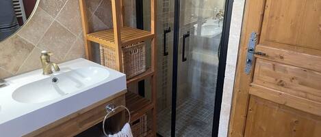 A bathroom with a wooden vanity, a glass shower enclosure, and a wooden door.