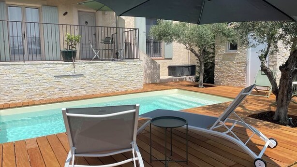 A wooden deck with a pool, lounge chairs, and a table.