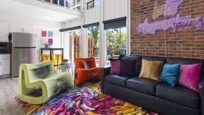 A modern living room with a black leather sofa, colorful cushions, a vibrant rug, and a neon sign on the brick wall. - Urban condo with loft office-community pool (Branson)