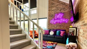 A staircase leading to a living area with a colorful rug, a black sofa with colorful cushions, and a neon sign on the wall. - Urban condo with loft office-community pool (Branson)