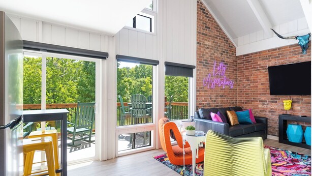 A spacious living area with a large window, a brick wall, a flat-screen TV, and a colorful rug. - Urban condo with loft office-community pool (Branson)