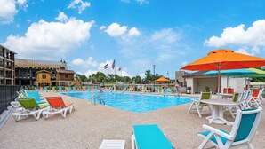 A pool area with lounge chairs and umbrellas, surrounded by buildings and flags. - Urban condo with loft office-community pool (Branson)