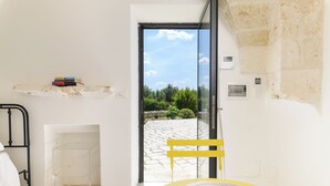 Une pièce donnant sur une cour intérieure, avec une chaise jaune, un lavabo blanc et une étagère remplie de livres.