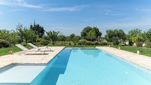 Une piscine rectangulaire à l’eau d’un bleu cristallin, entourée d’une terrasse en sable et dot ée de chaises longues.